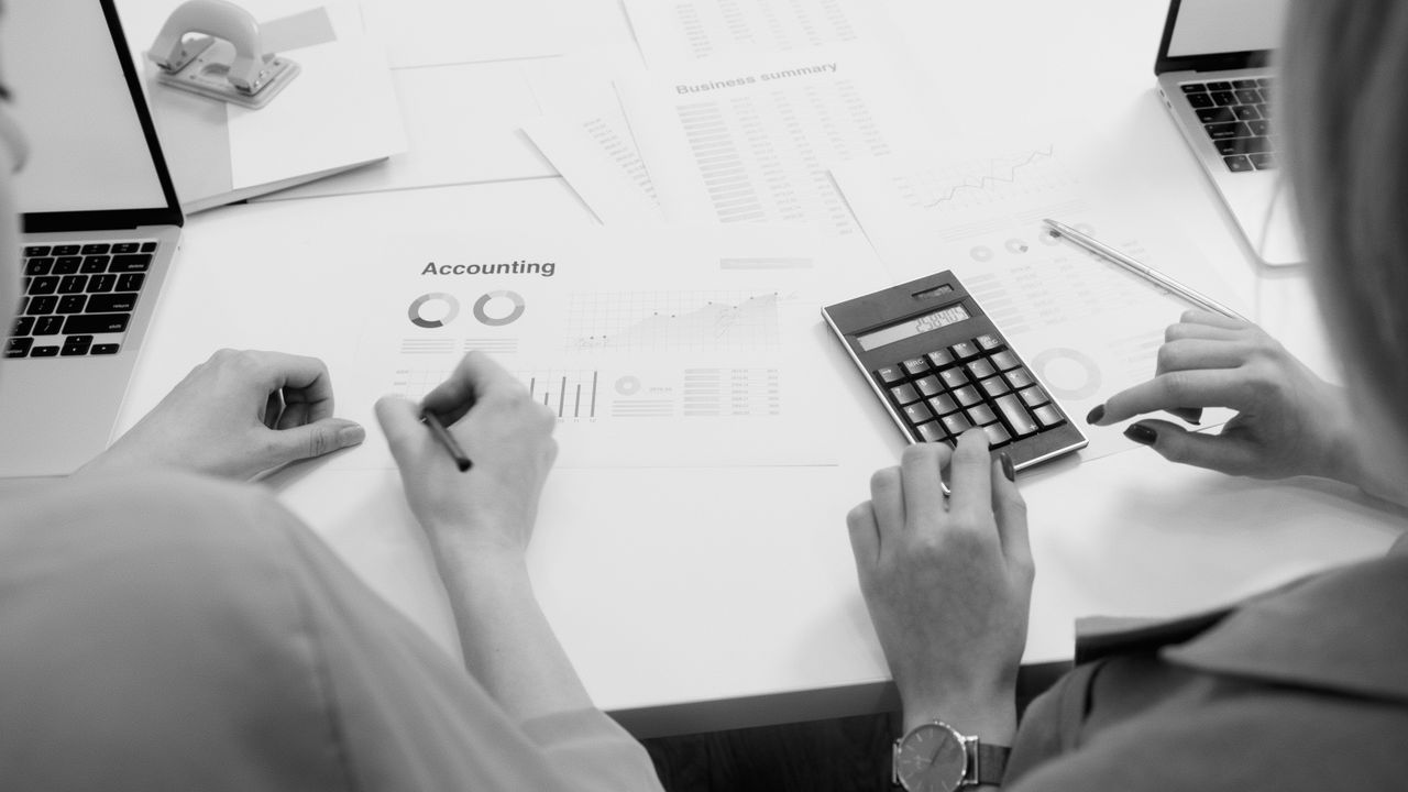 Crafting Captivating Headlines: Your awesome post title goes here Black and white office scene featuring accounting documents, calculator, and laptops.