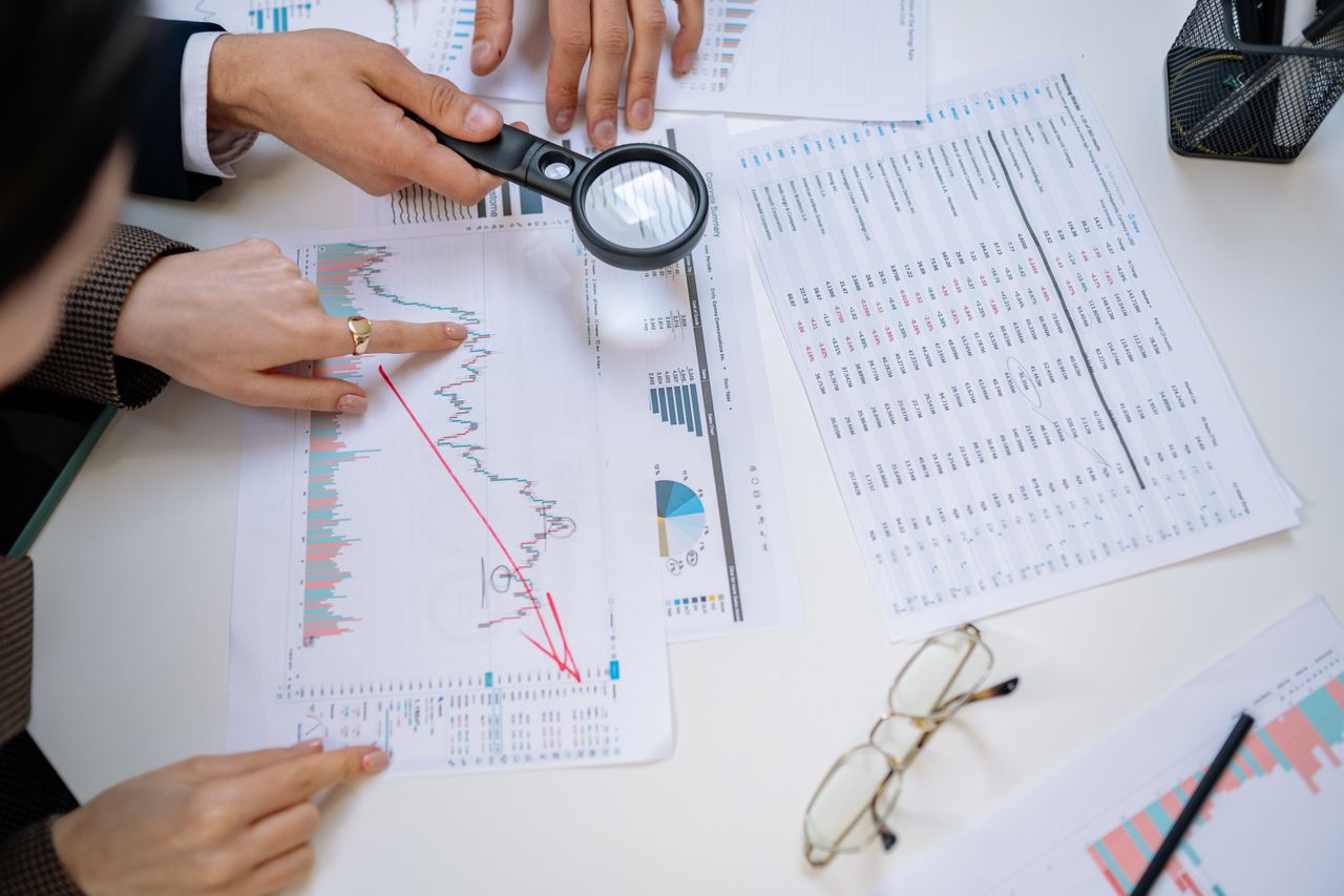 Mastering the First Impression: Your intriguing post title goes here Business professionals examining financial documents with magnifying glass for detailed analysis.